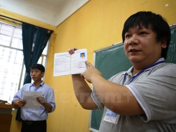  Cán bộ coi thi hướng dẫn thí sinh làm thủ tục dự thi trung học phổ thông quốc gia. (Ảnh: Lê Minh Sơn/Vietnam+)